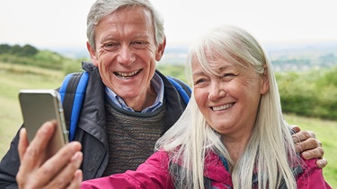 Ein älterer Mann und eine ältere Frau sind beim Wandern unterwegs. Sie machen ein Selfie mit dem Smartphone. | Bild: colourbox.com